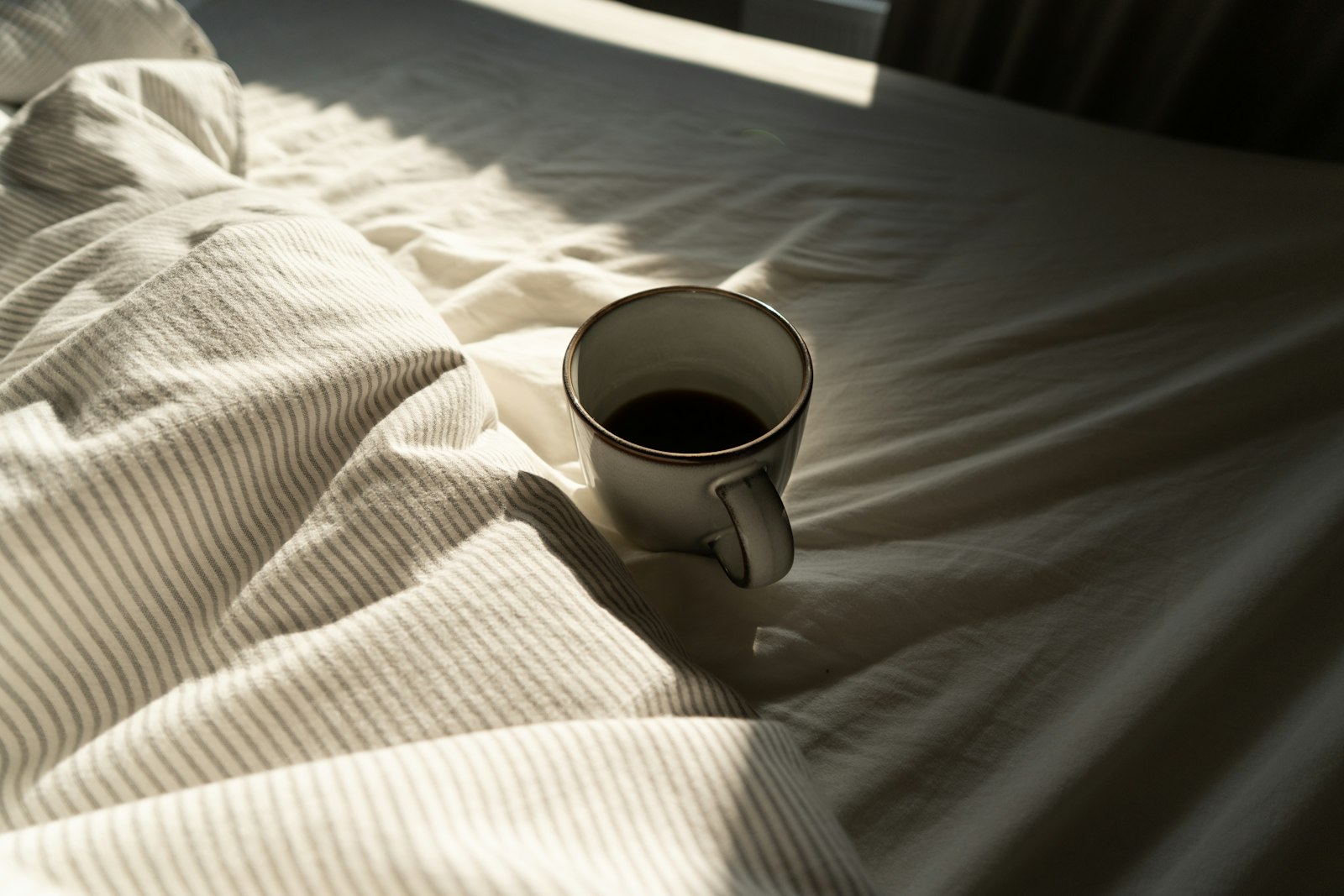 A mug of coffee on white bedding in morning light